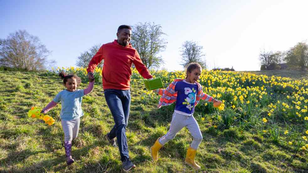 Man and two daughters running through a meadow